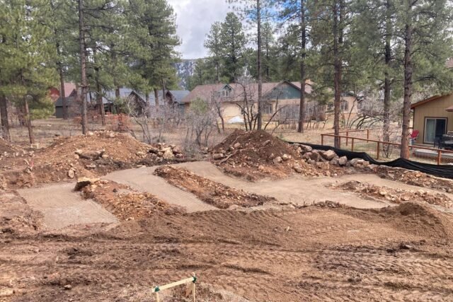 a dirt pit with trees and houses in the background