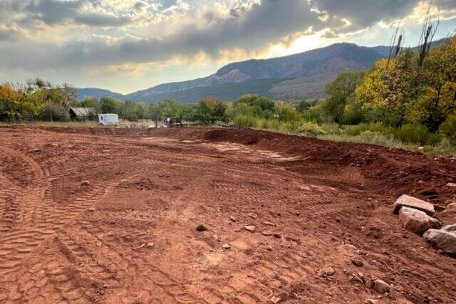 a dirt field with trees and mountains in the background